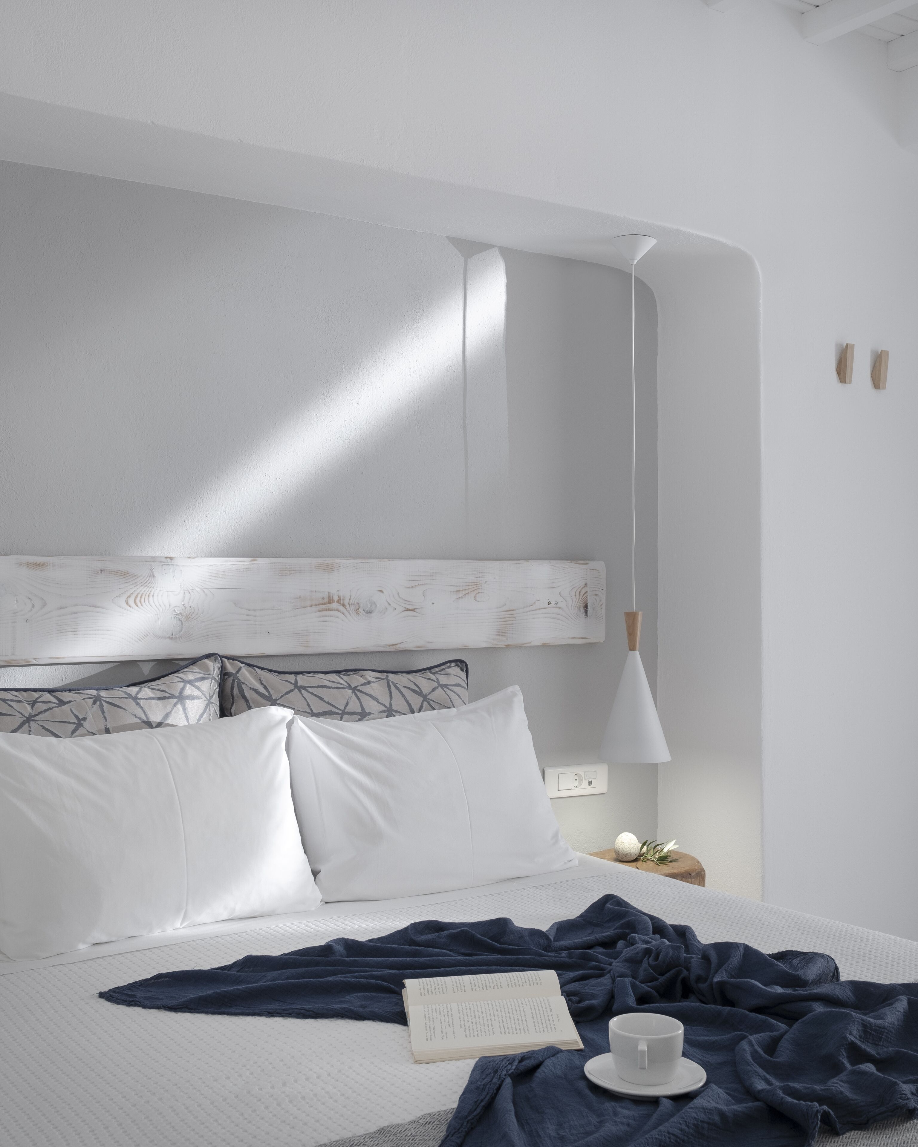 A neatly made bed with a white headboard, a bedside table with a lamp, and a book and cup on the bed.