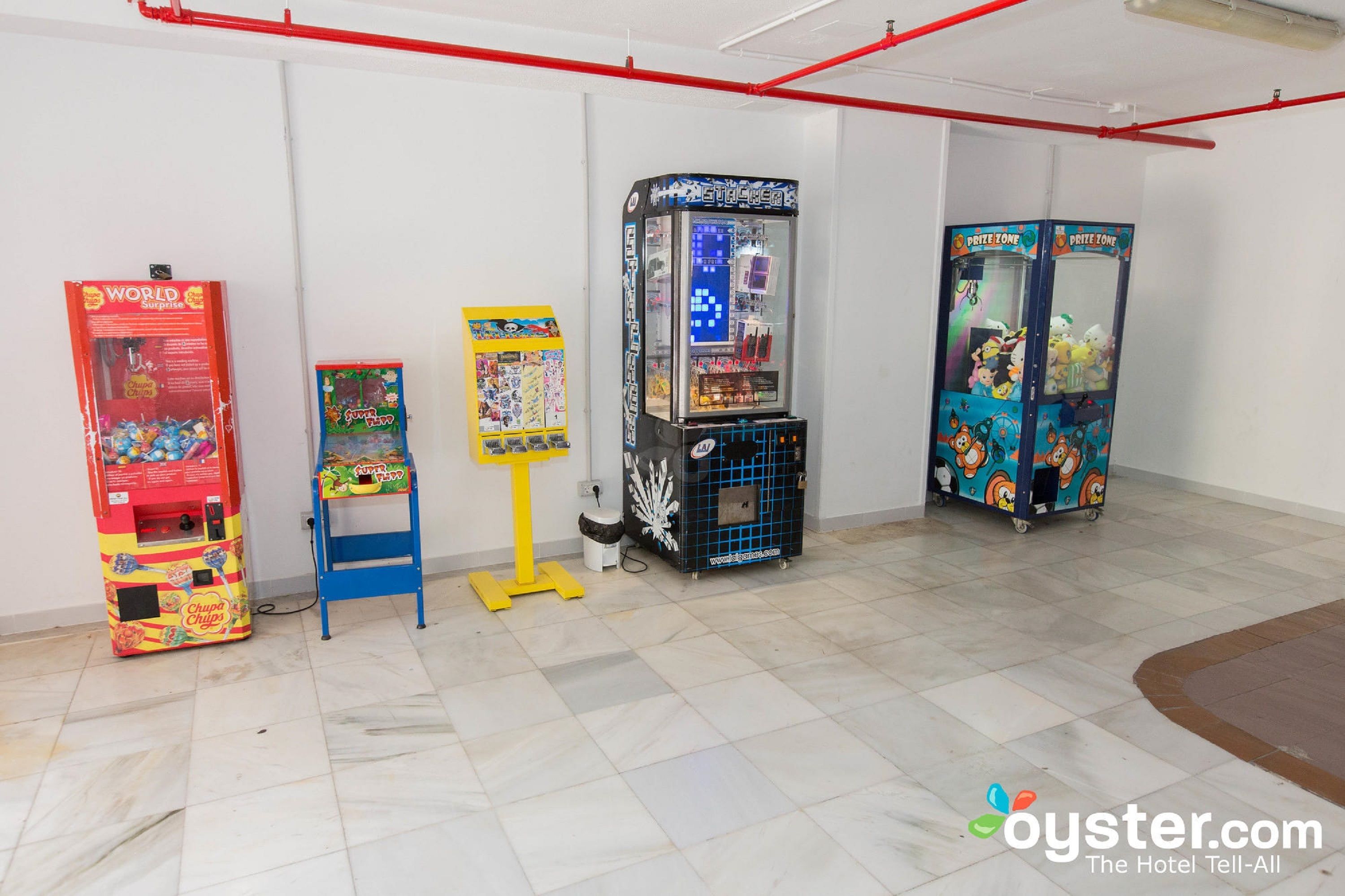Una habitación con cuatro máquinas de arcade, un cartel publicitario azul y una máquina expendedora roja.