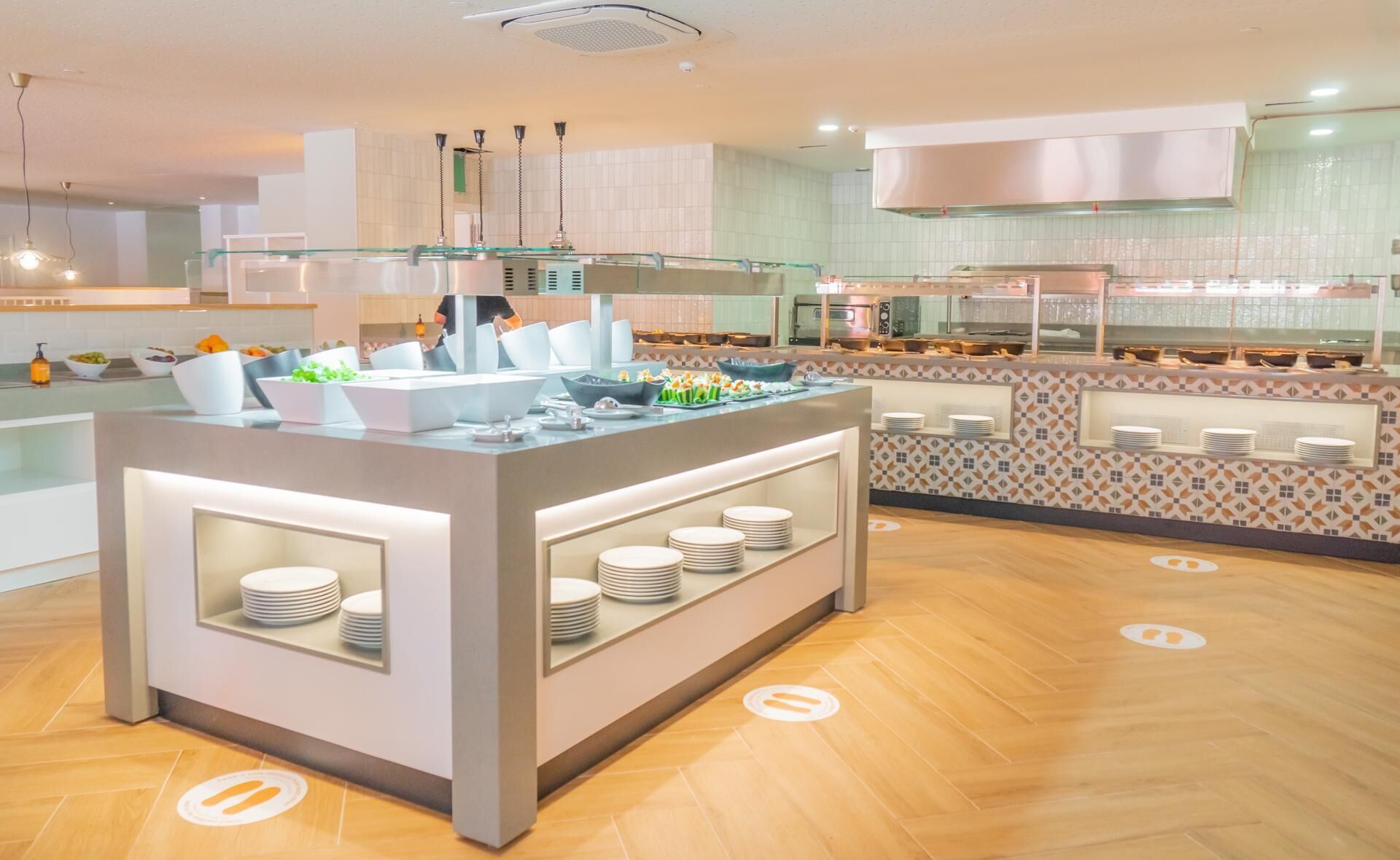 A modern buffet setup with a central island, multiple serving stations, and a kitchen area in the background.