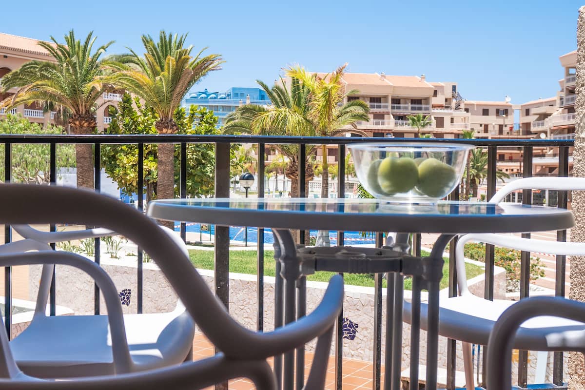 A balcony with a glass table and chairs, overlooking a pool and palm trees.