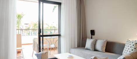 A modern living room with a sofa, a coffee table, and a balcony with a view of the outdoors.
