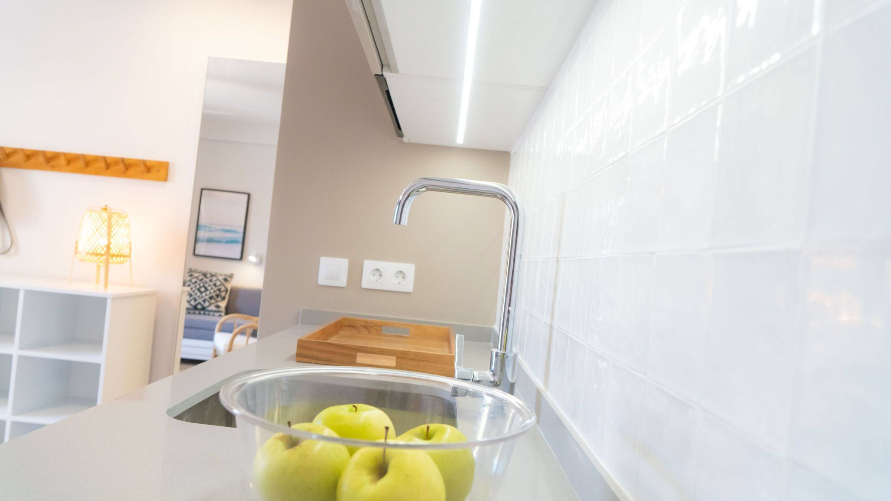 A modern kitchen with a stainless steel sink, a wooden cutting board, and a bowl of green apples.