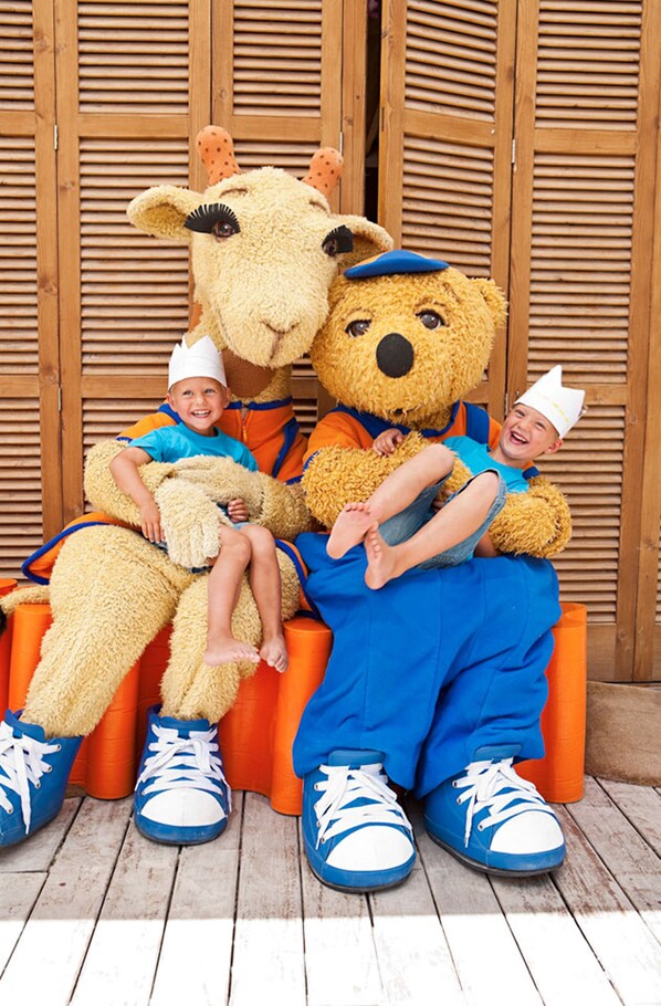 To børn sidder på orange trin med en stor bamse imellem sig.