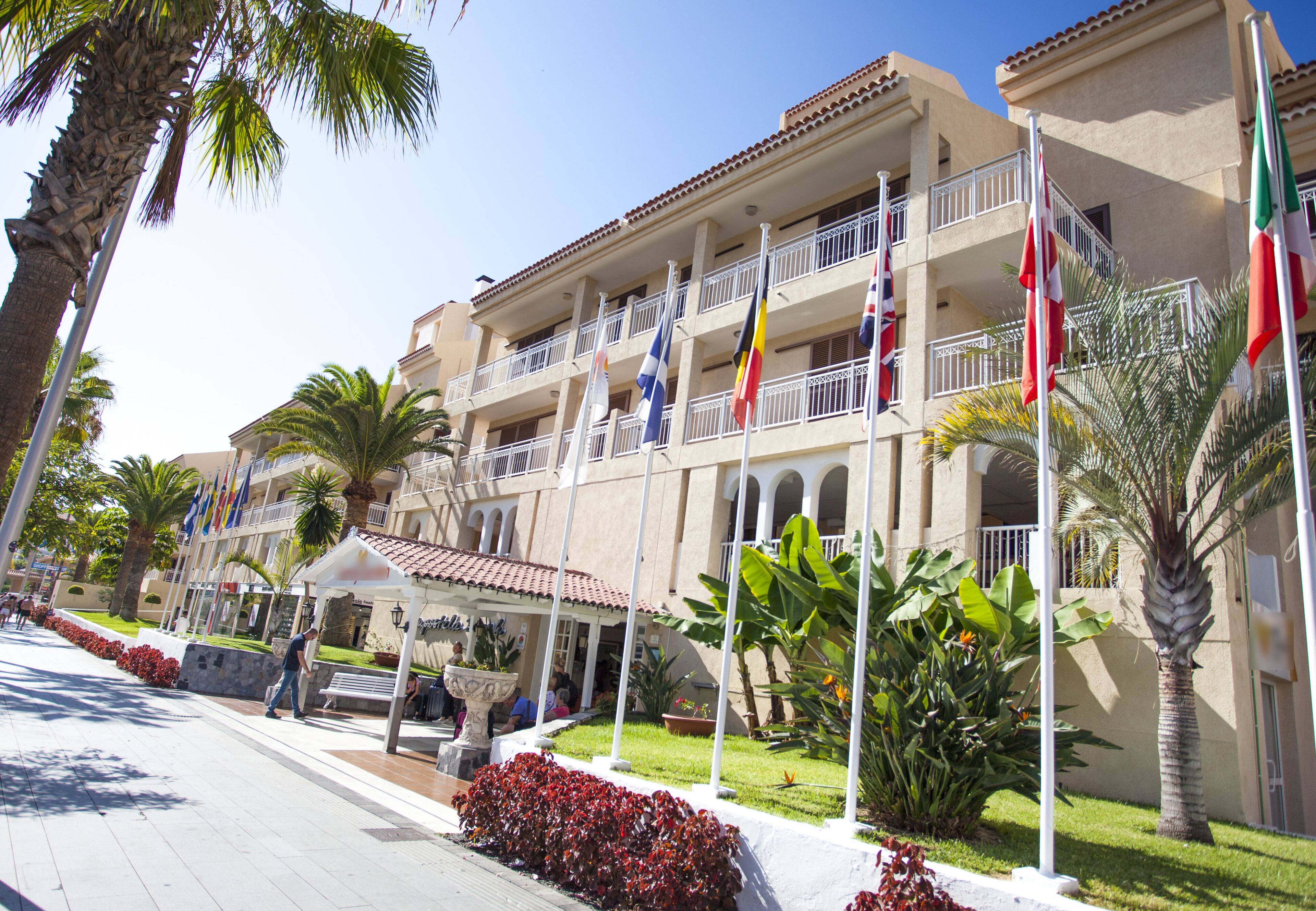 Een hotel met meerdere balkons, vlaggen en palmbomen.