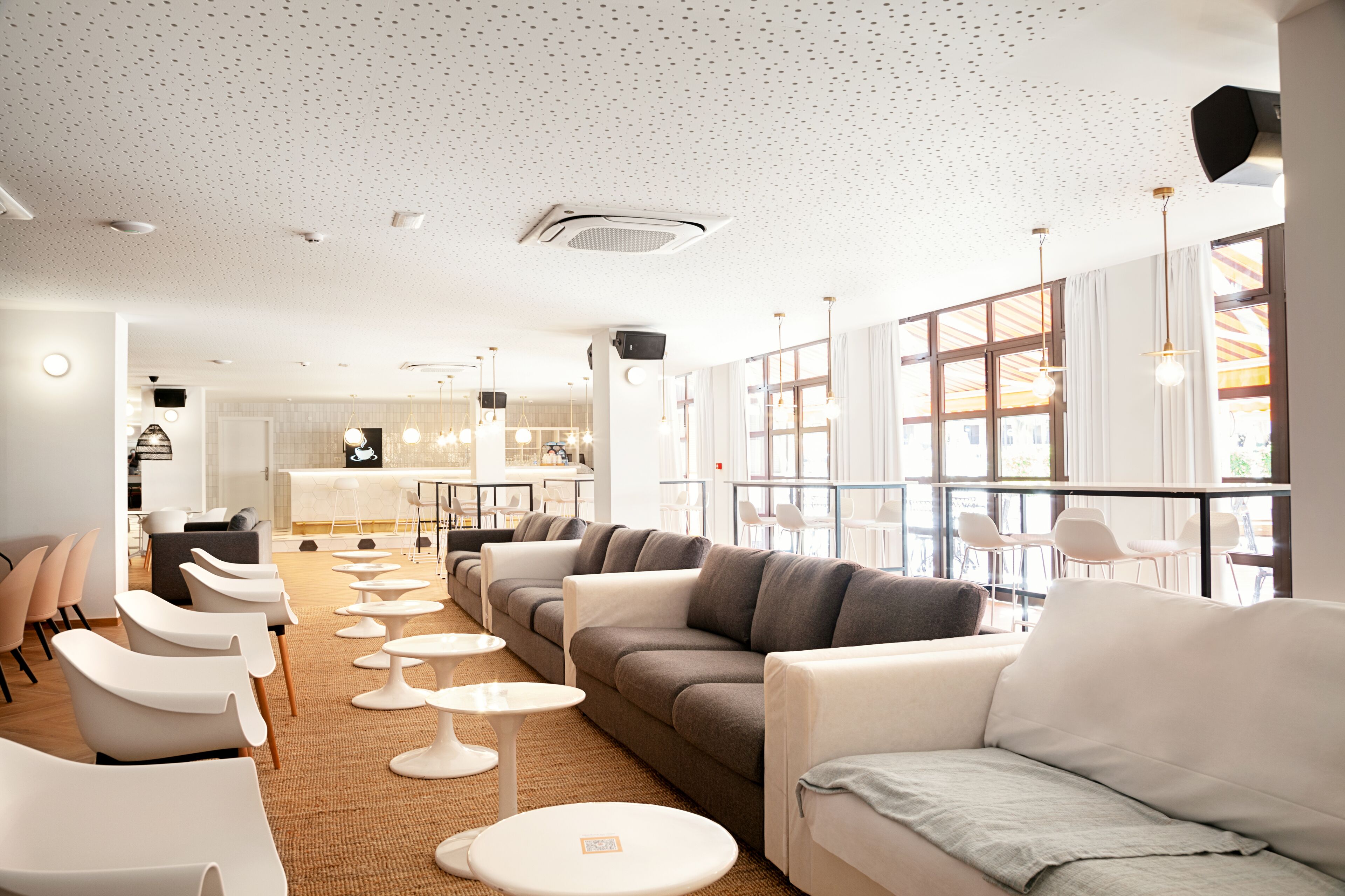 A modern hotel lobby with a seating area, a kitchen, and large windows.