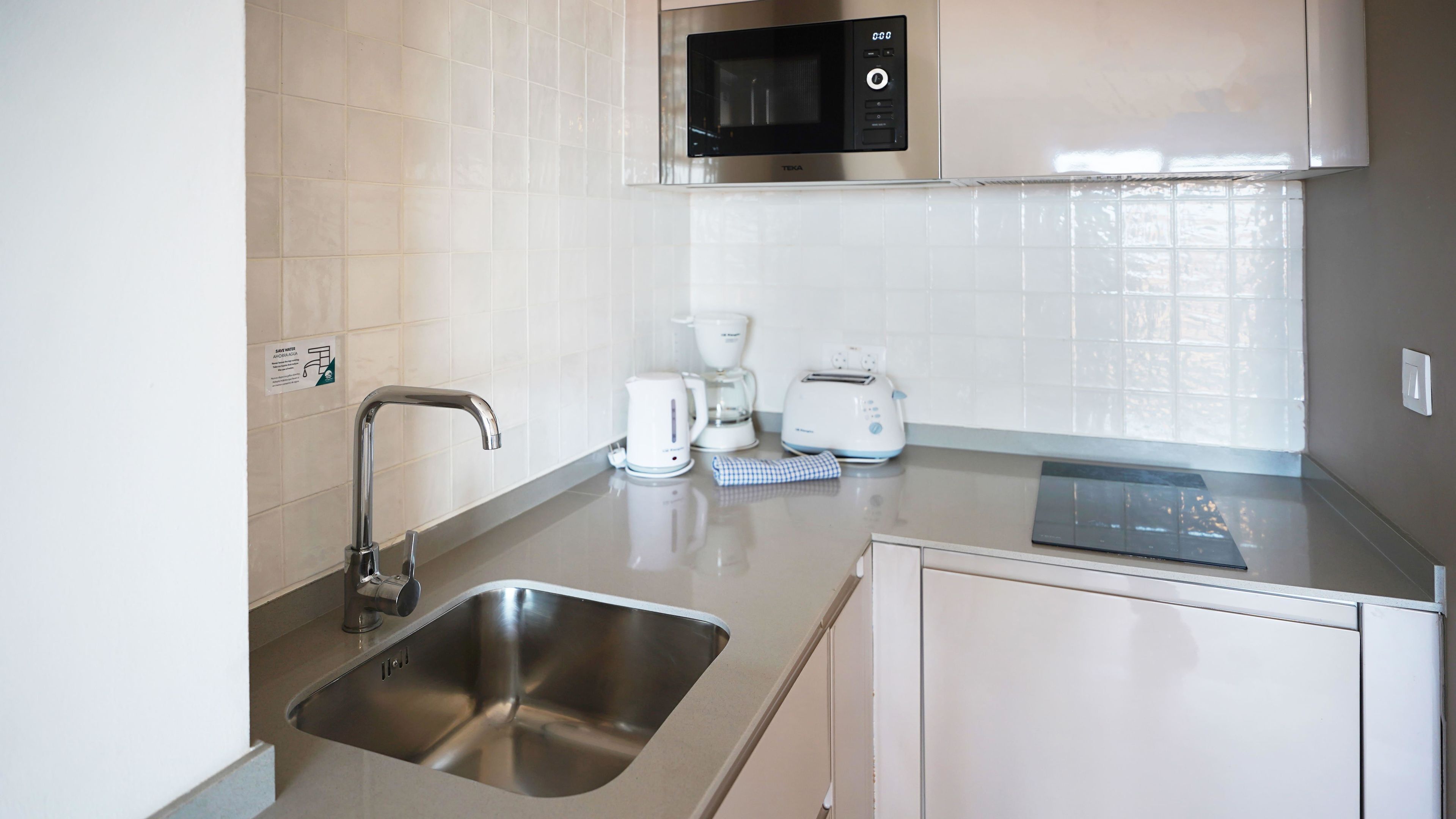 A modern kitchen with a stainless steel sink, a microwave, a coffee maker, and a toaster.