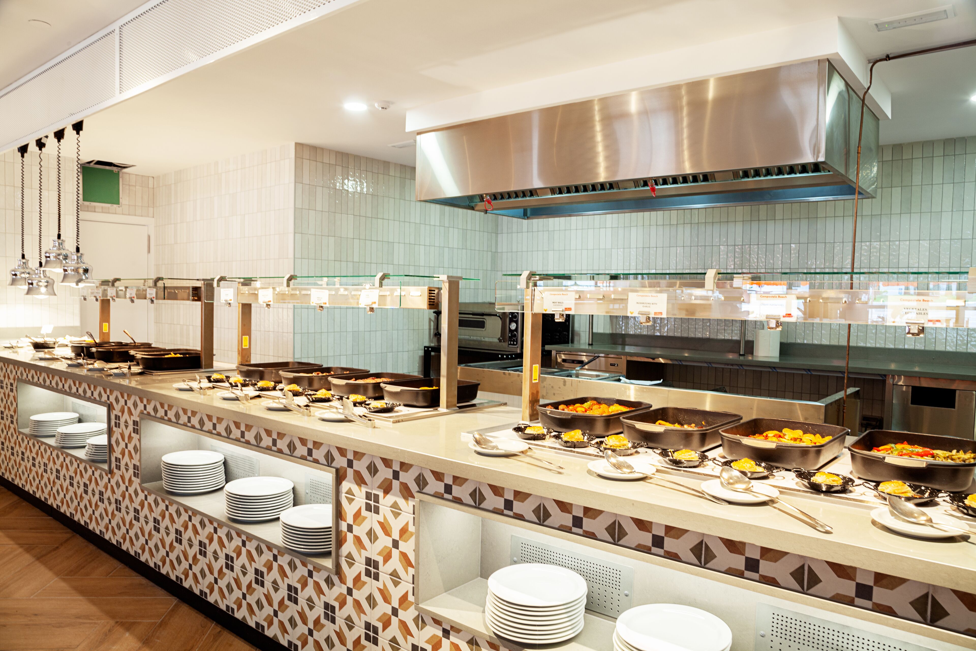 Een buffetopstelling met diverse themastations, roestvrijstalen apparatuur en een betegelde spatwand.