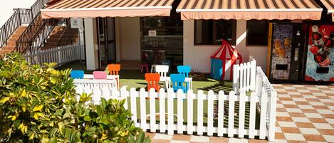 A courtyard with a white picket fence, outdoor seating area with colorful chairs, and a vending machine.