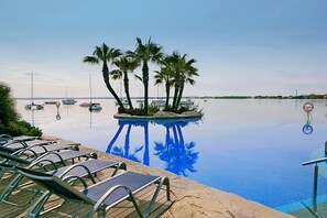 Una piscina con sillas de descanso, palmeras y barcos en el agua.