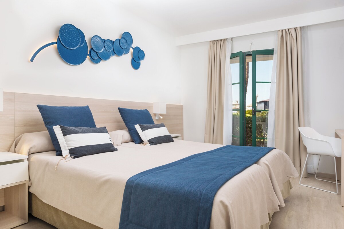 A modern hotel room with a large bed, two nightstands, a desk, and a chair.