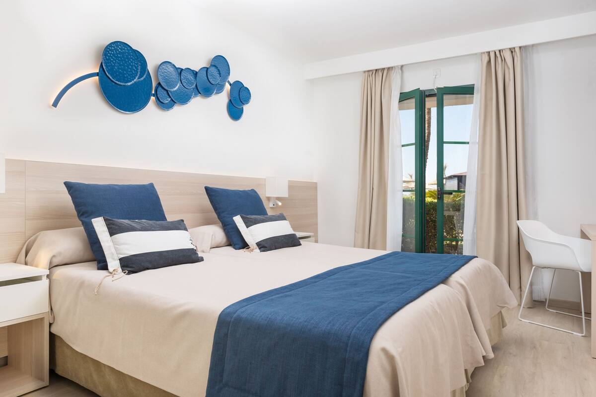 A modern hotel room with a large bed, two nightstands, a desk, and a chair.