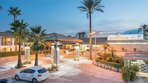 A hotel entrance with a covered walkway, palm trees, and a sign reading "Alcudia Mar Club". - Alcudiamar Marina Residence (Alcúdia)