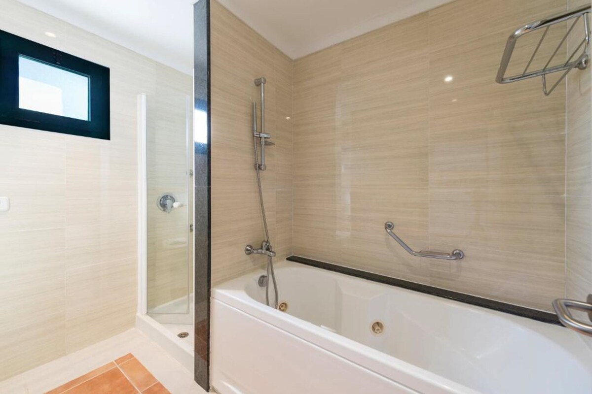A modern bathroom with a glass-enclosed shower, a bathtub, and a handrail.
