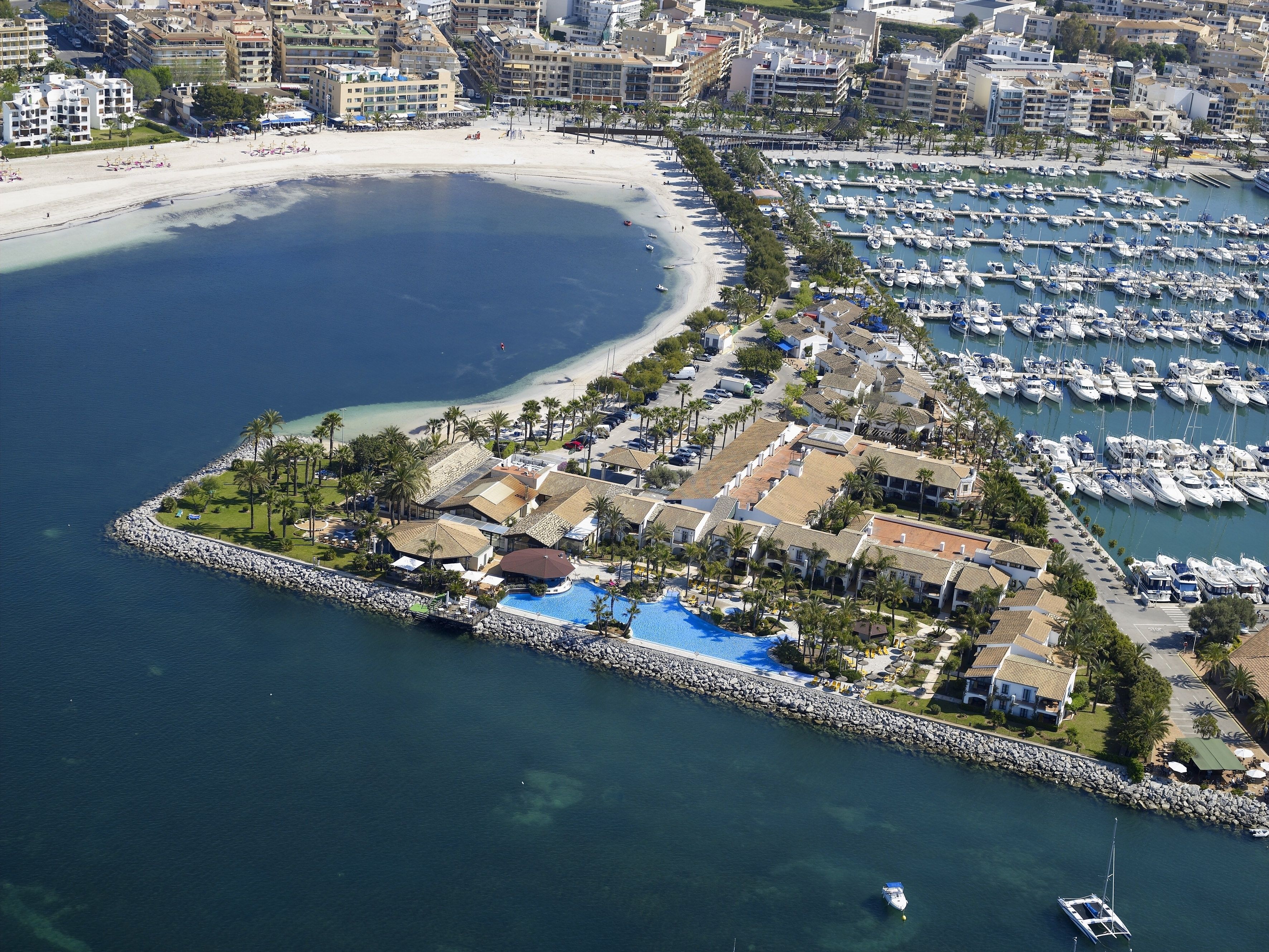 Ein Luftbild eines Küstenresorts mit einer Marina, Strand und einer kleinen Insel mit Pool.