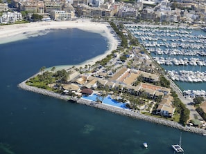 Vue aérienne d’une station balnéaire dotée d’un port de plaisance, d’une plage et d’une petite île avec une piscine.