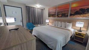 Habitación de hotel con cama, mesitas de noche, escritorio, silla y un amplio ventanal con cortinas.