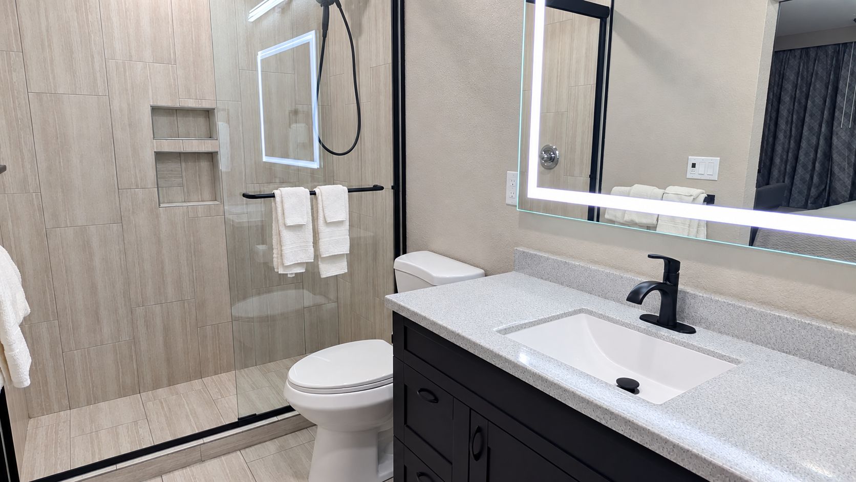 A modern bathroom with a glass shower enclosure, a white toilet, a vanity with a sink, and a large mirror.