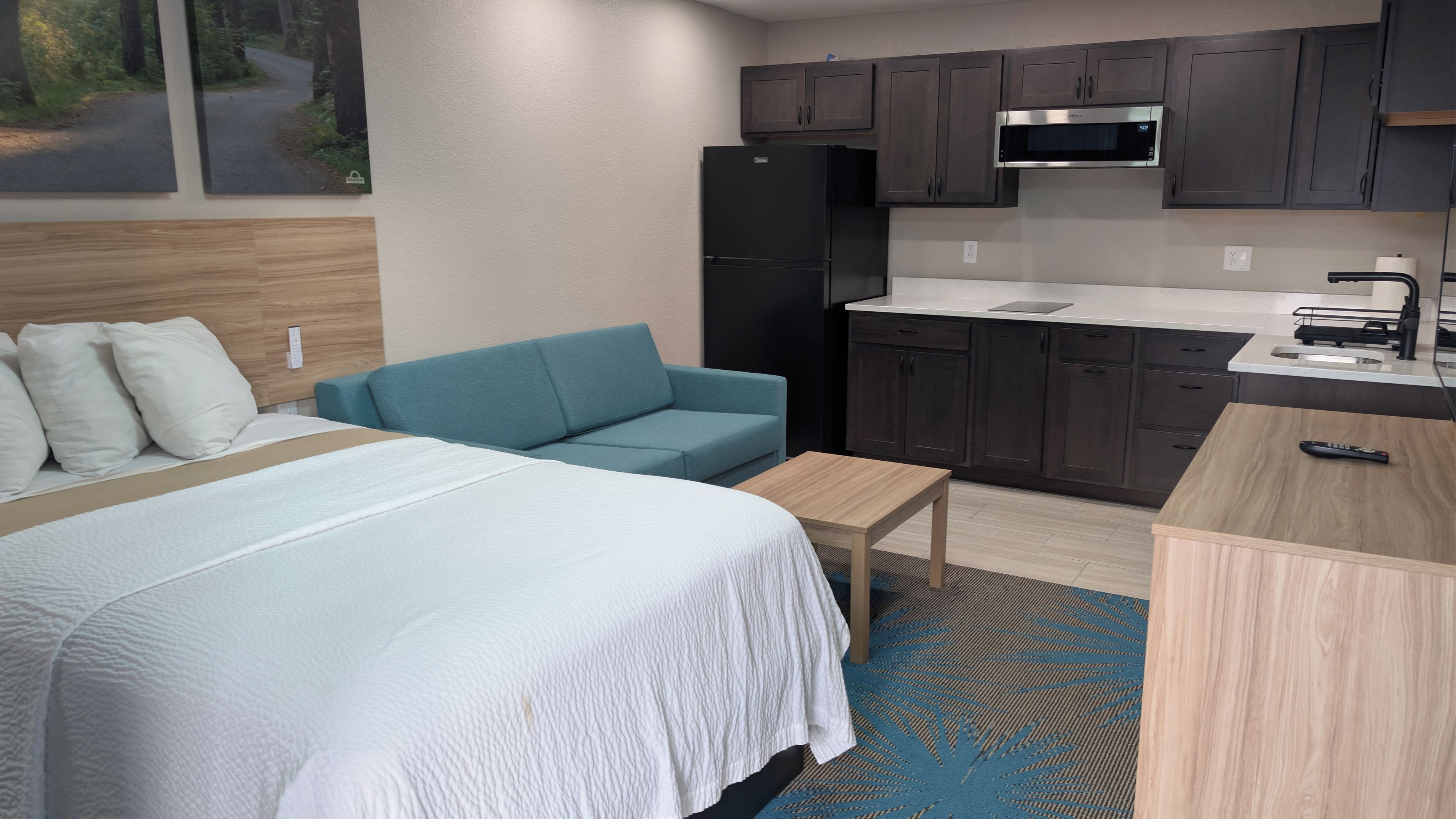 A hotel room with a bed, a sofa, a small table, a kitchenette with a microwave, and cabinets.