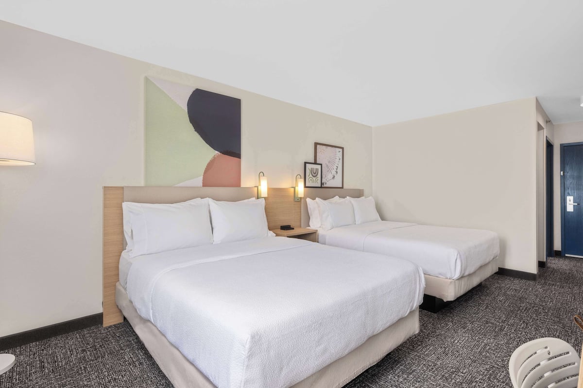 A hotel room with two beds, a large abstract painting, and a door to the right.