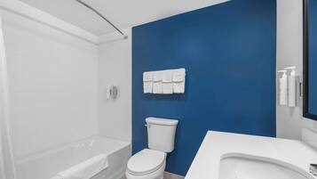 A modern bathroom with a white bathtub, a white toilet, and a blue accent wall.