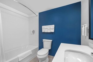 Un baño moderno con una bañera blanca, un inodoro blanco y una pared azul decorativa.