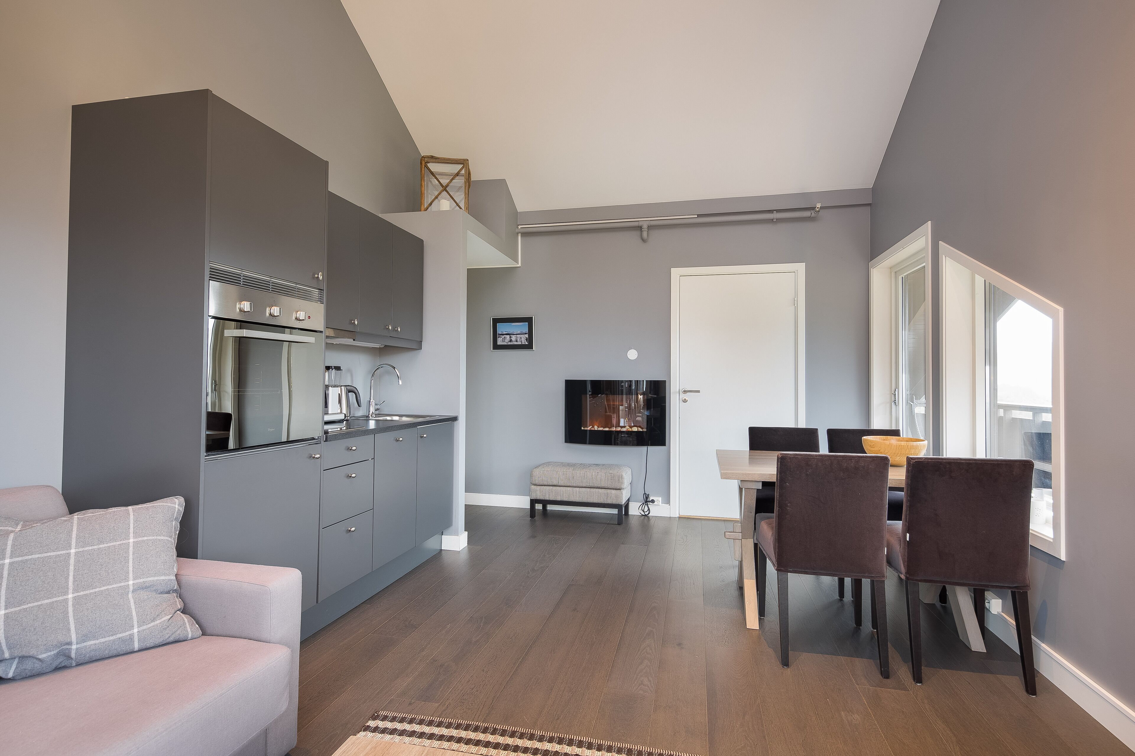 Une cuisine moderne avec des meubles gris, un coin repas avec une table et des chaises, et un espace de vie avec un canapé.