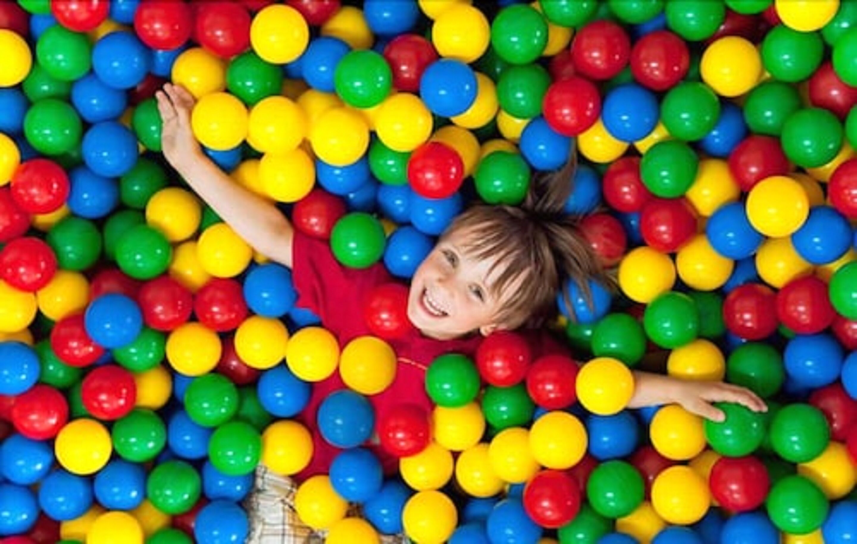 Un niño acostado en un chapoteadero lleno de bolas multicolores.