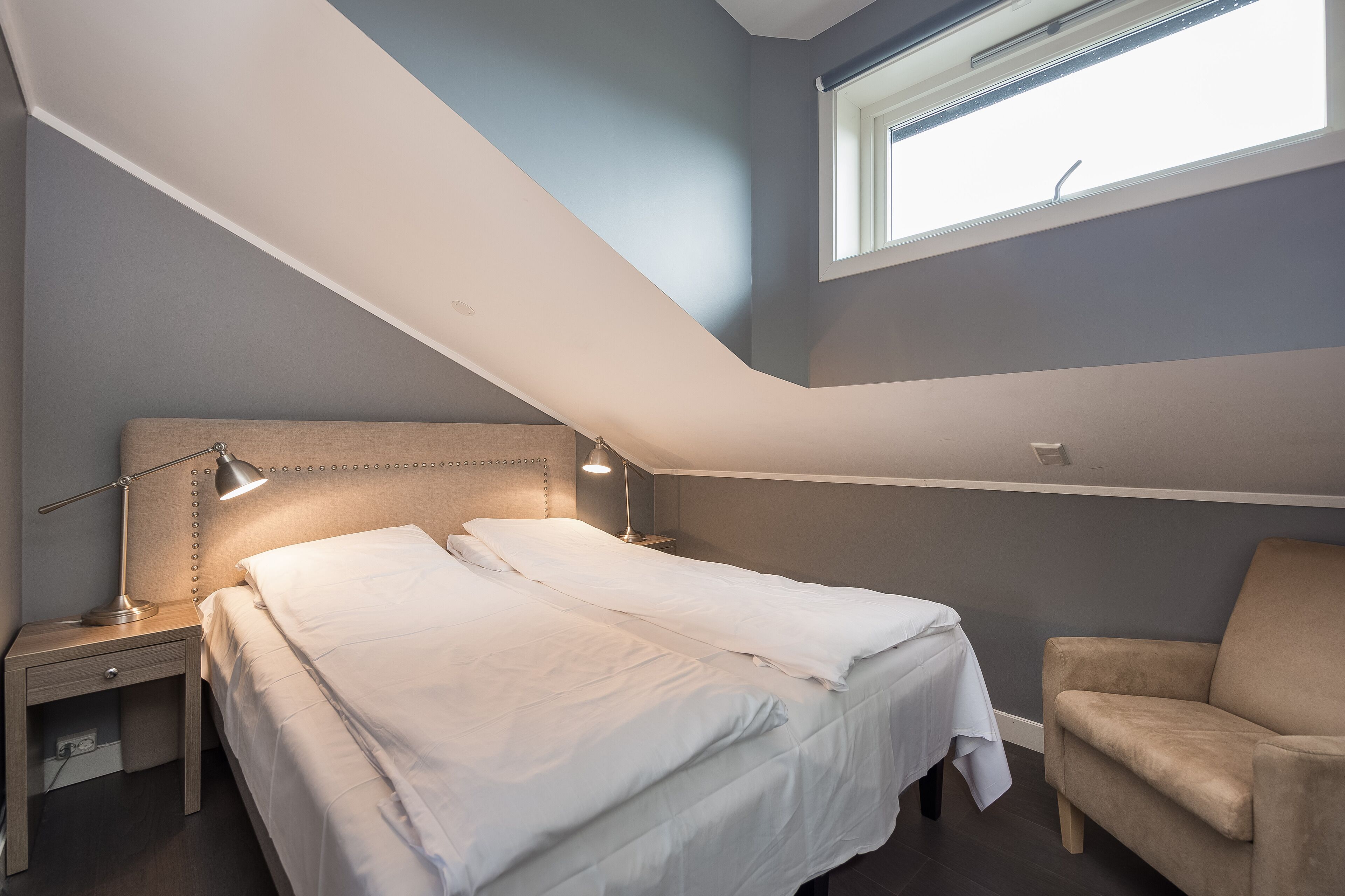 A bedroom with a bed, bedside table, lamp, and a chair.