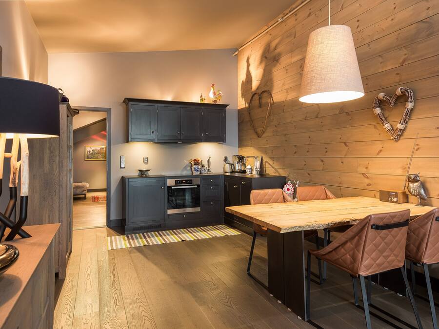 A modern kitchen with dark cabinets, a wooden dining table, and a heart-shaped decoration on the wall.