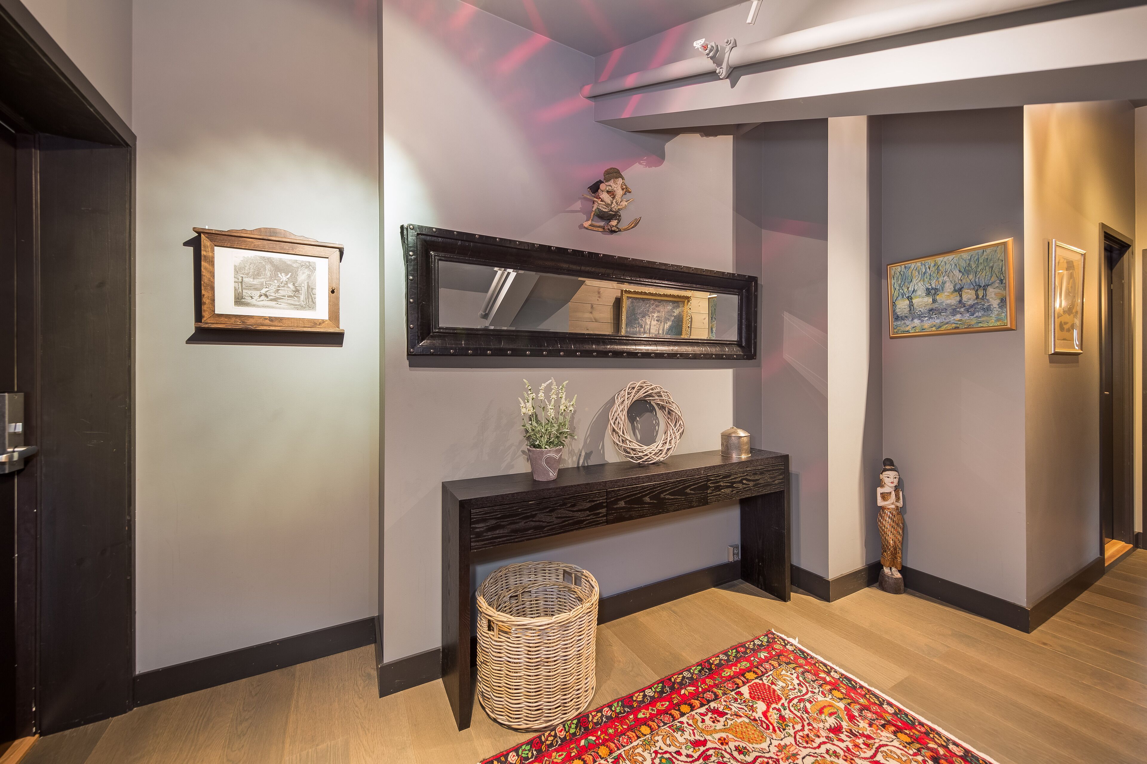 A hallway with a dark console table, a large mirror, and a decorative basket.
