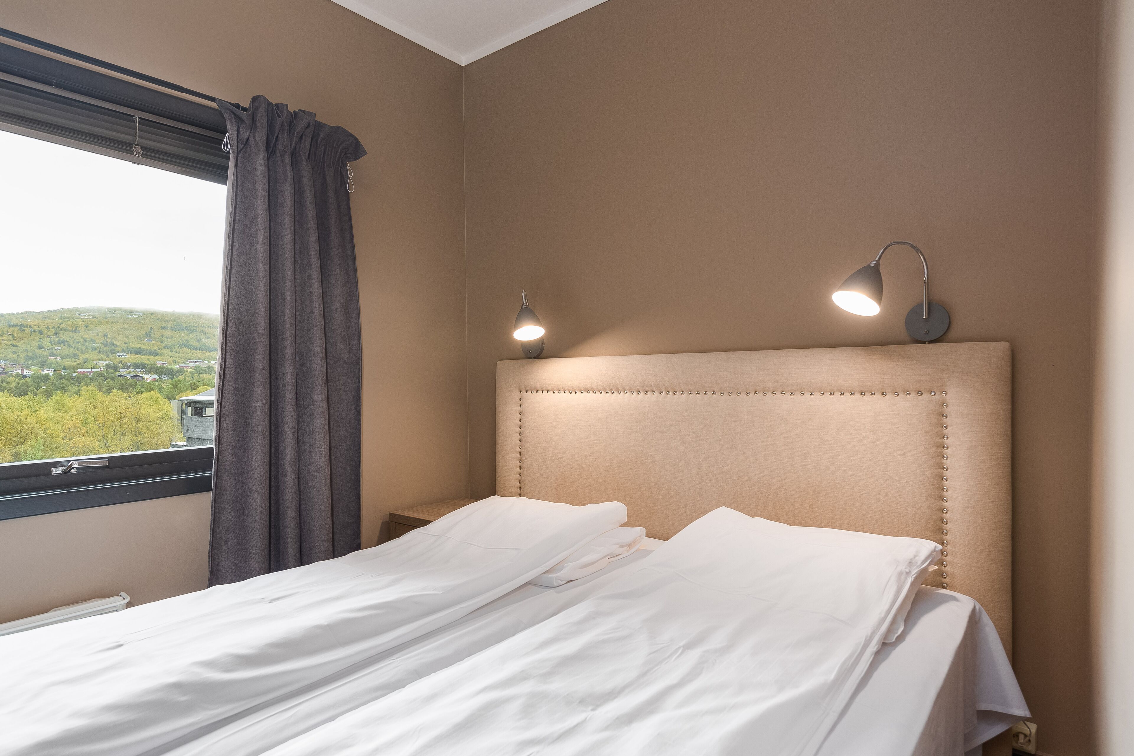 A neatly made bed with white linens, a headboard with a row of buttons, and two bedside lamps.