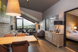 A modern room with a wooden dining table, cushioned chairs, a sofa, a bed, and a large window offering a city view. - Highland Lodge (Hol)