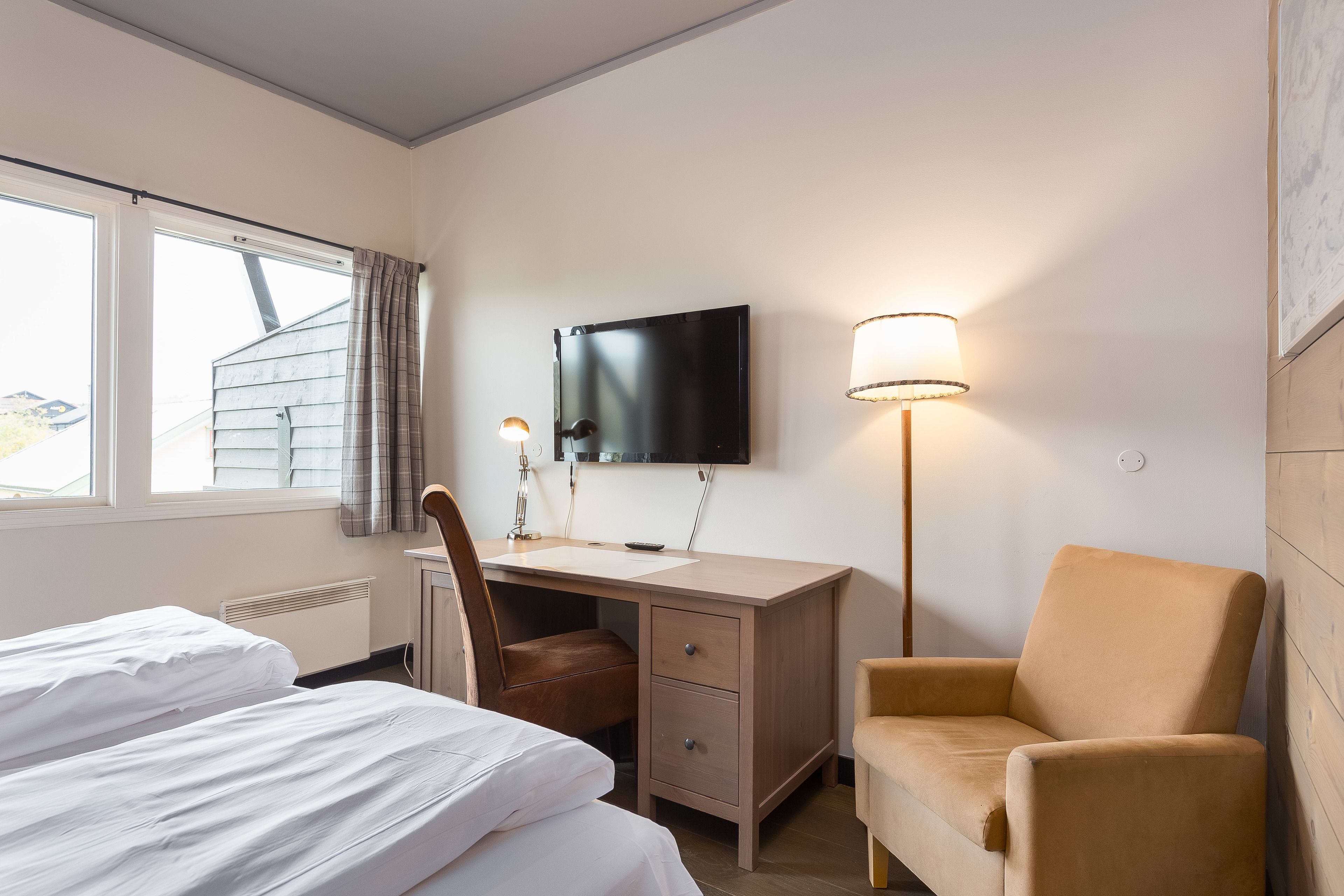 A hotel room with two beds, a desk with a chair, a TV, and a lamp.
