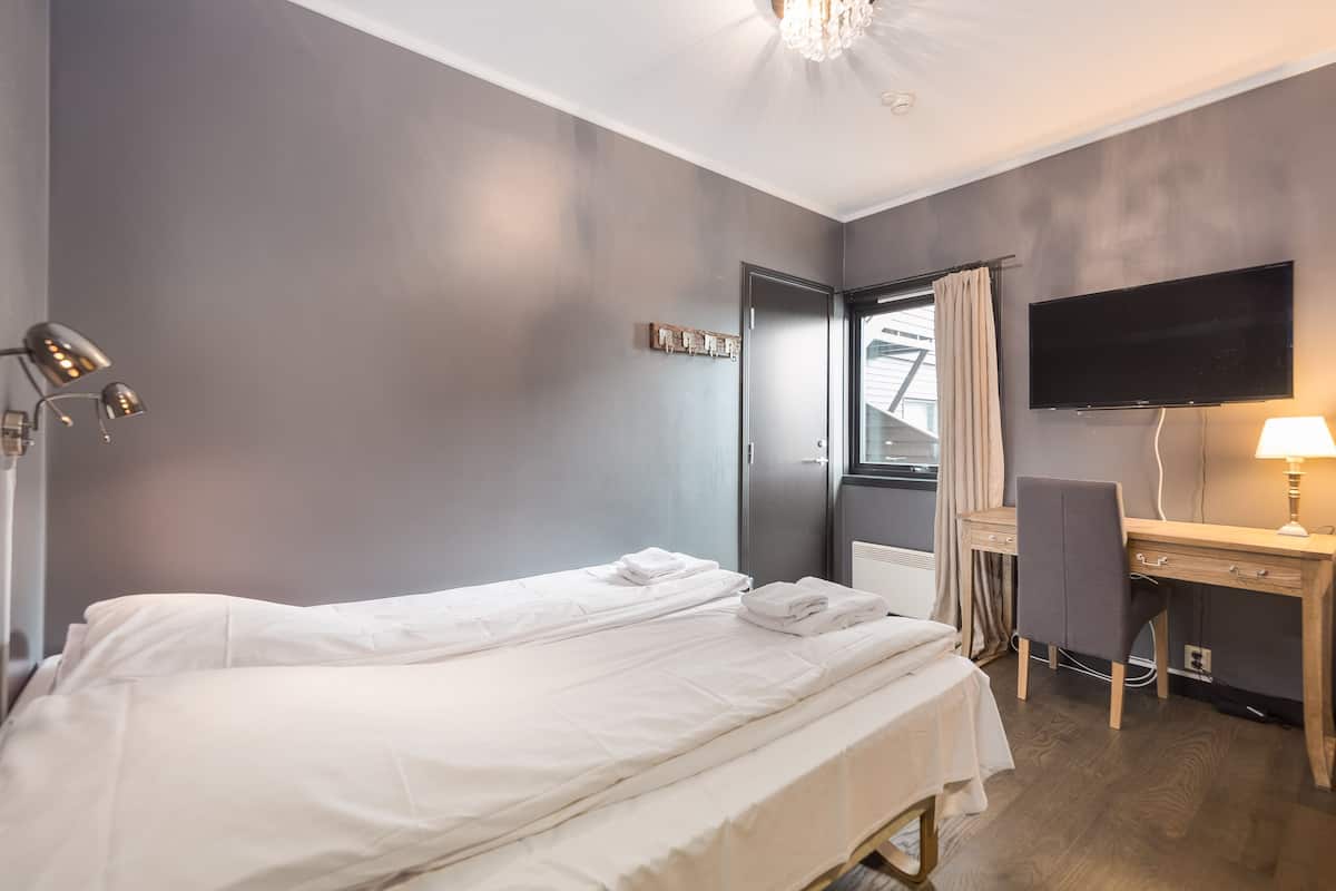 A hotel room with a single bed, a desk with a chair, a flat-screen TV, and a lamp.