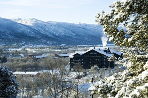 A lodge with a prominent sign, surrounded by snow-covered trees and mountains in the background. - Highland Lodge (Hol)