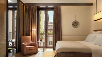 Habitación de hotel con una cama grande, un área de estar con una silla y una mesita, y vistas al exterior por una puerta corredera.