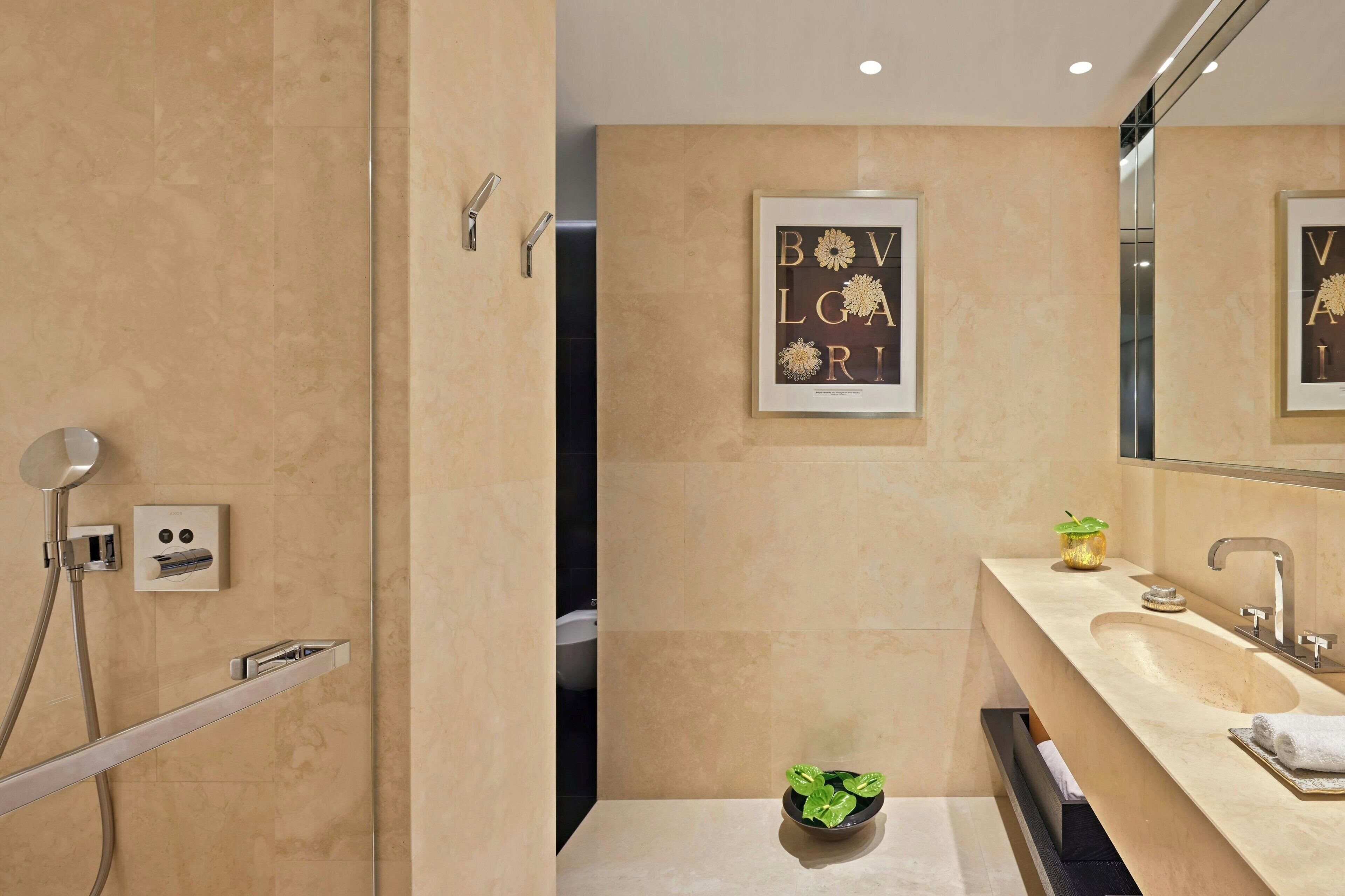 A modern bathroom with a beige tiled wall, a framed artwork, a sink with a mirror, and a shower area.