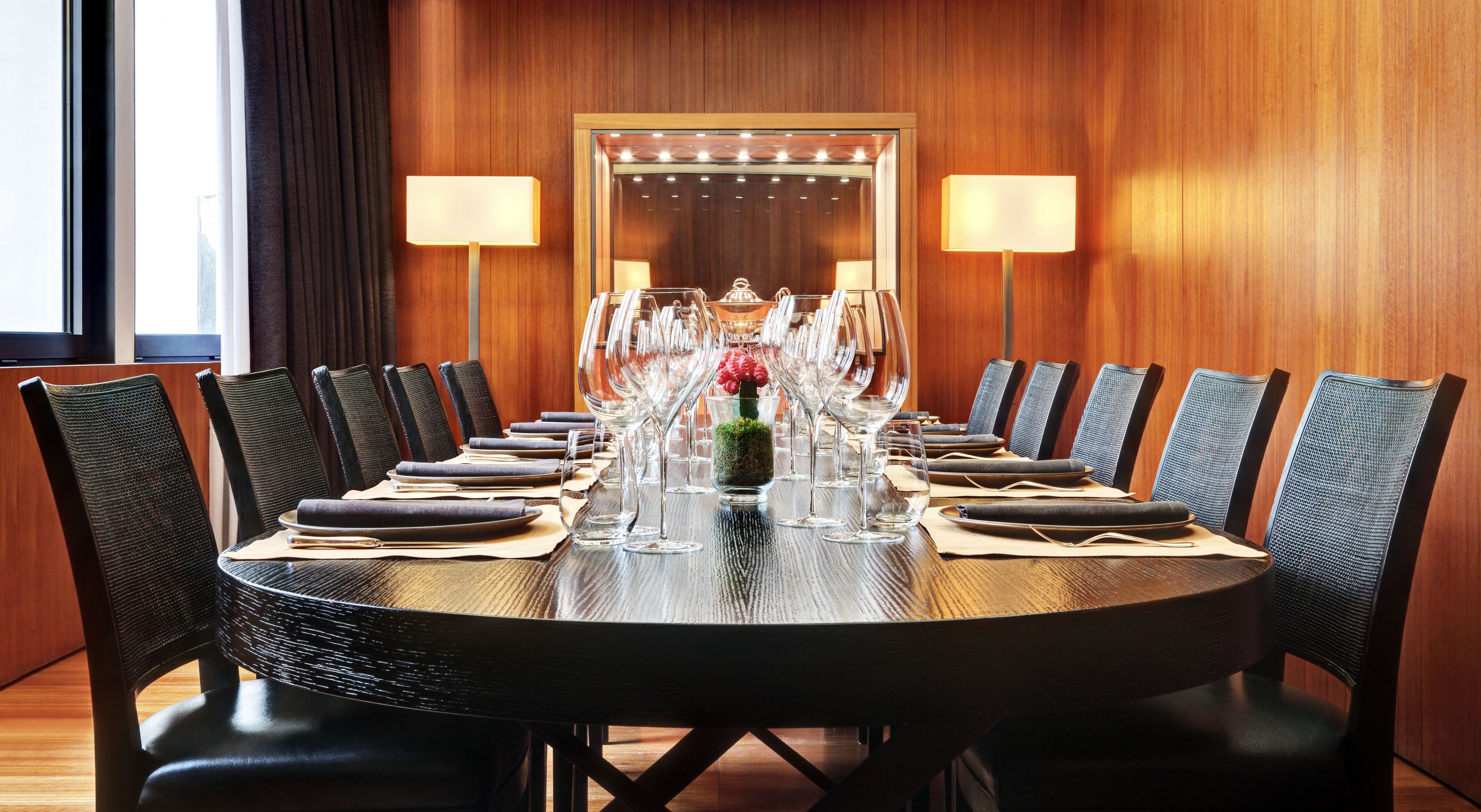 Un salón de conferencias con una mesa redonda, sillas y un jarrón con flores.