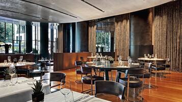 A spacious dining area with multiple tables and chairs, large windows, and a modern ceiling design.