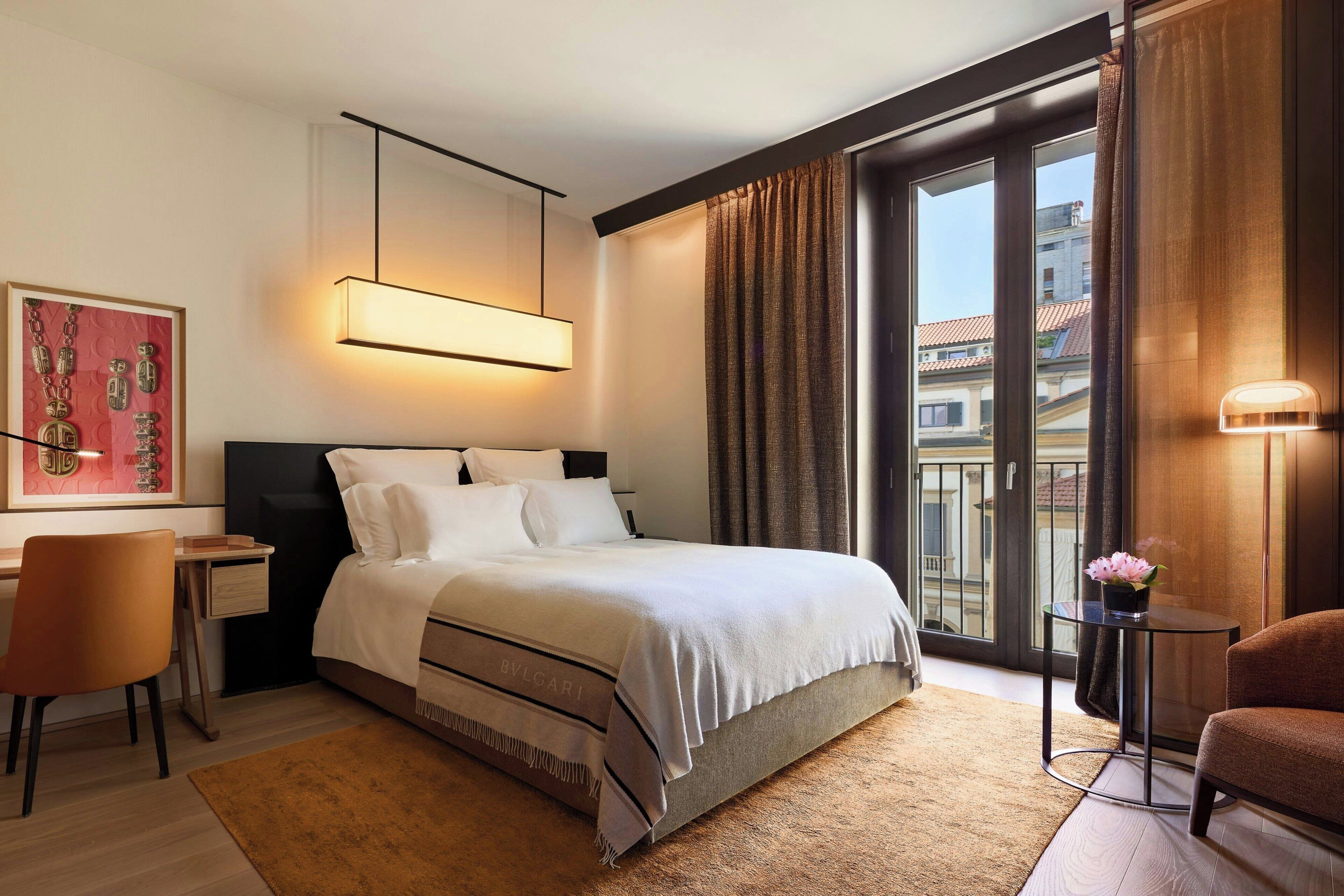 Une chambre d’hôtel moderne, dotée d’un grand lit, d’un bureau, d’une chaise et offrant une vue sur la ville par la fenêtre.