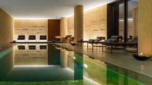 Un espace piscine intérieur moderne, doté de chaises longues et d’une eau cristalline.