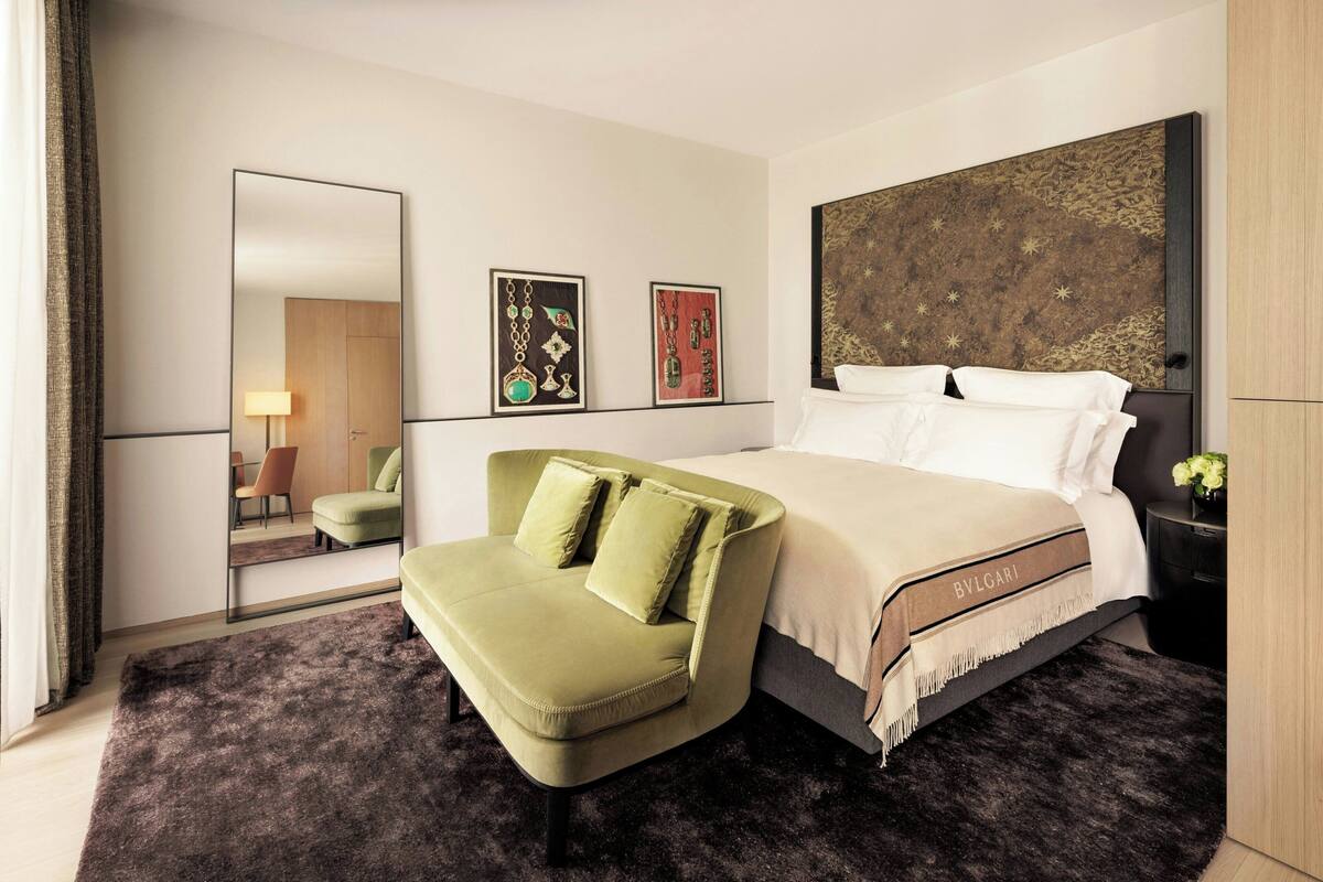A hotel room with a bed, a green sofa, a large mirror, and artwork on the wall.