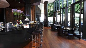 Un espace bar moderne, doté d’un comptoir élégant, de tabourets et offrant une vue sur l’extérieur grâce à de grandes fenêtres.