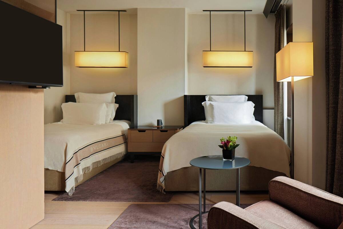 A hotel room with two beds, a TV, a small table with a plant, and a sofa.