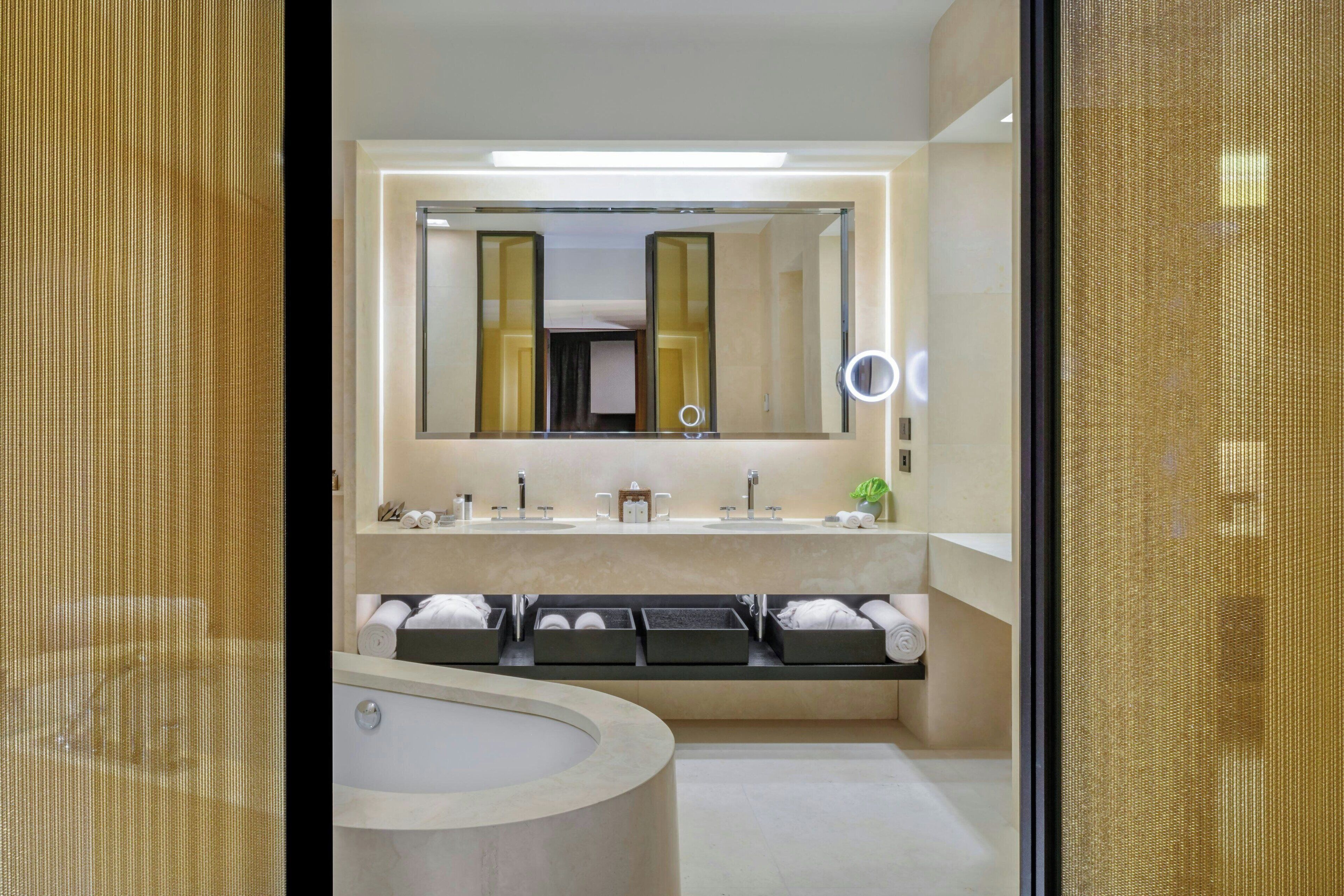 Een moderne badkamer met een grote spiegel, twee wasbakken, een badkuip en een wastafelmeubel met opbergladen.
