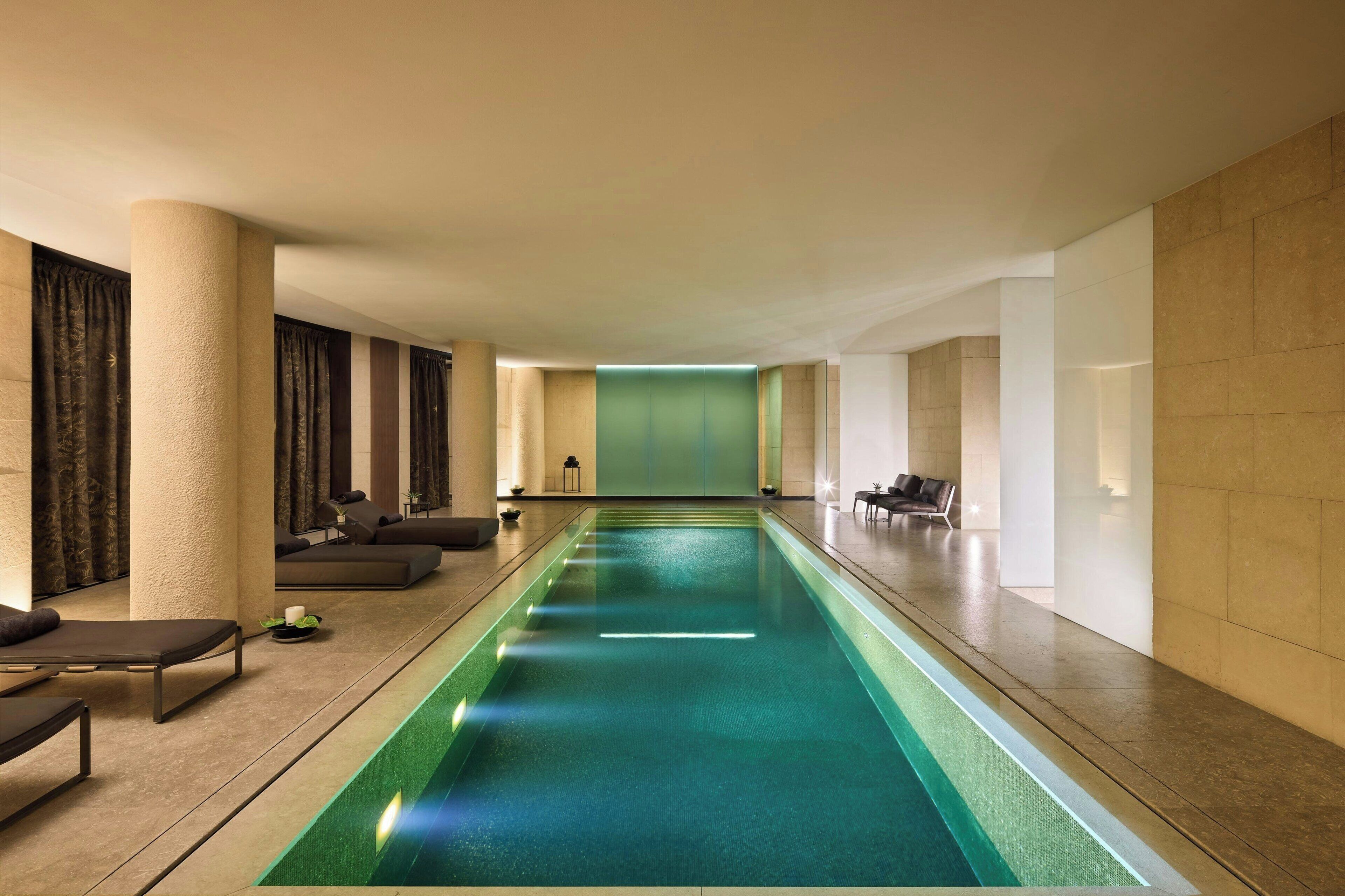 Una larga piscina interior con diseño moderno, rodeada de zonas de descanso con mobiliario y una paleta de colores neutros.