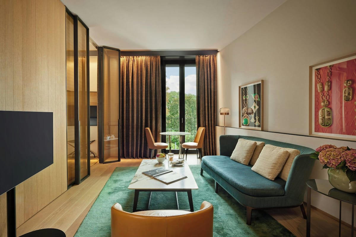 A modern hotel room with a large window, a sofa, a coffee table, and a TV.