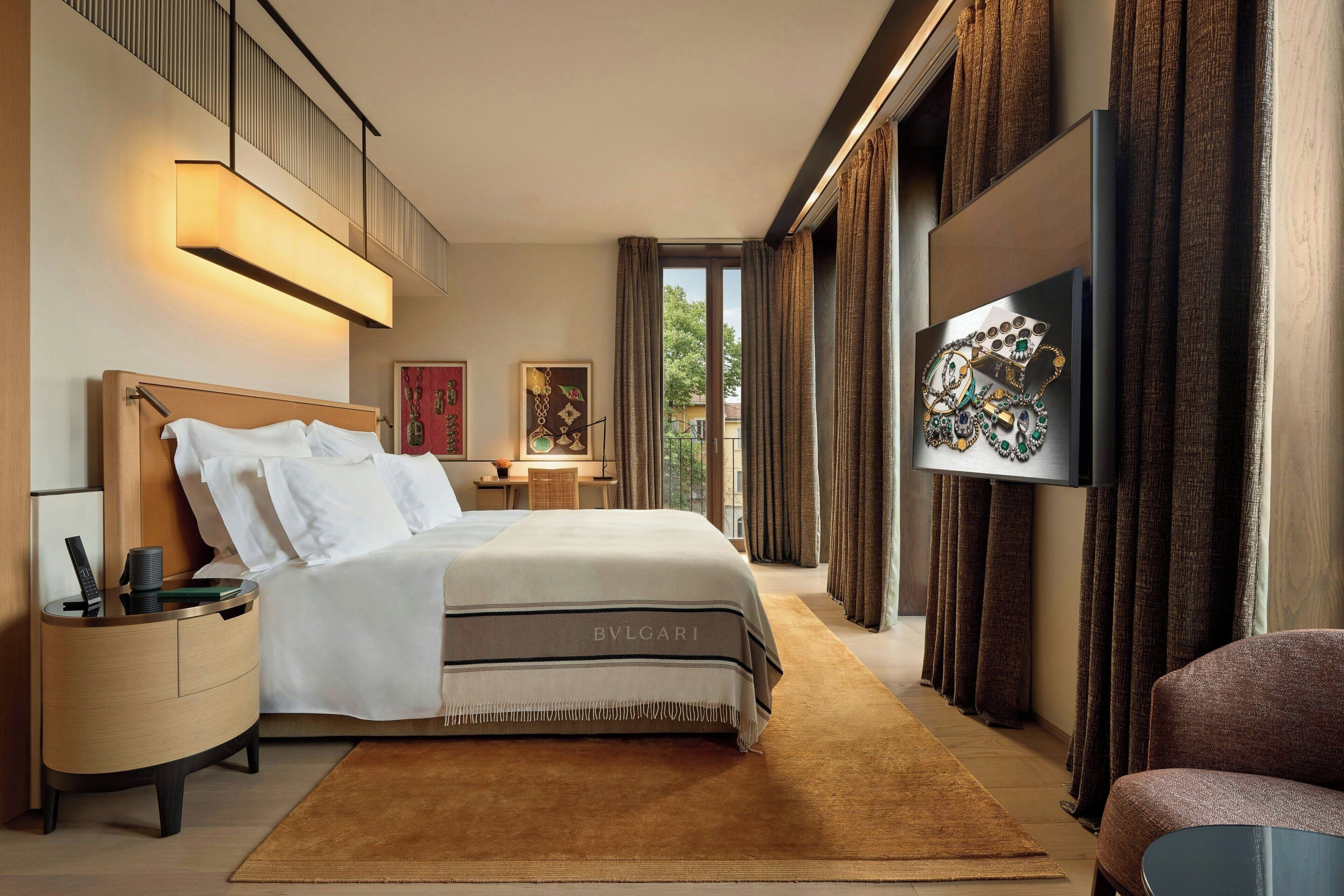 A modern hotel room with a large bed, a flat-screen TV, a nightstand, and a view of the outdoors.