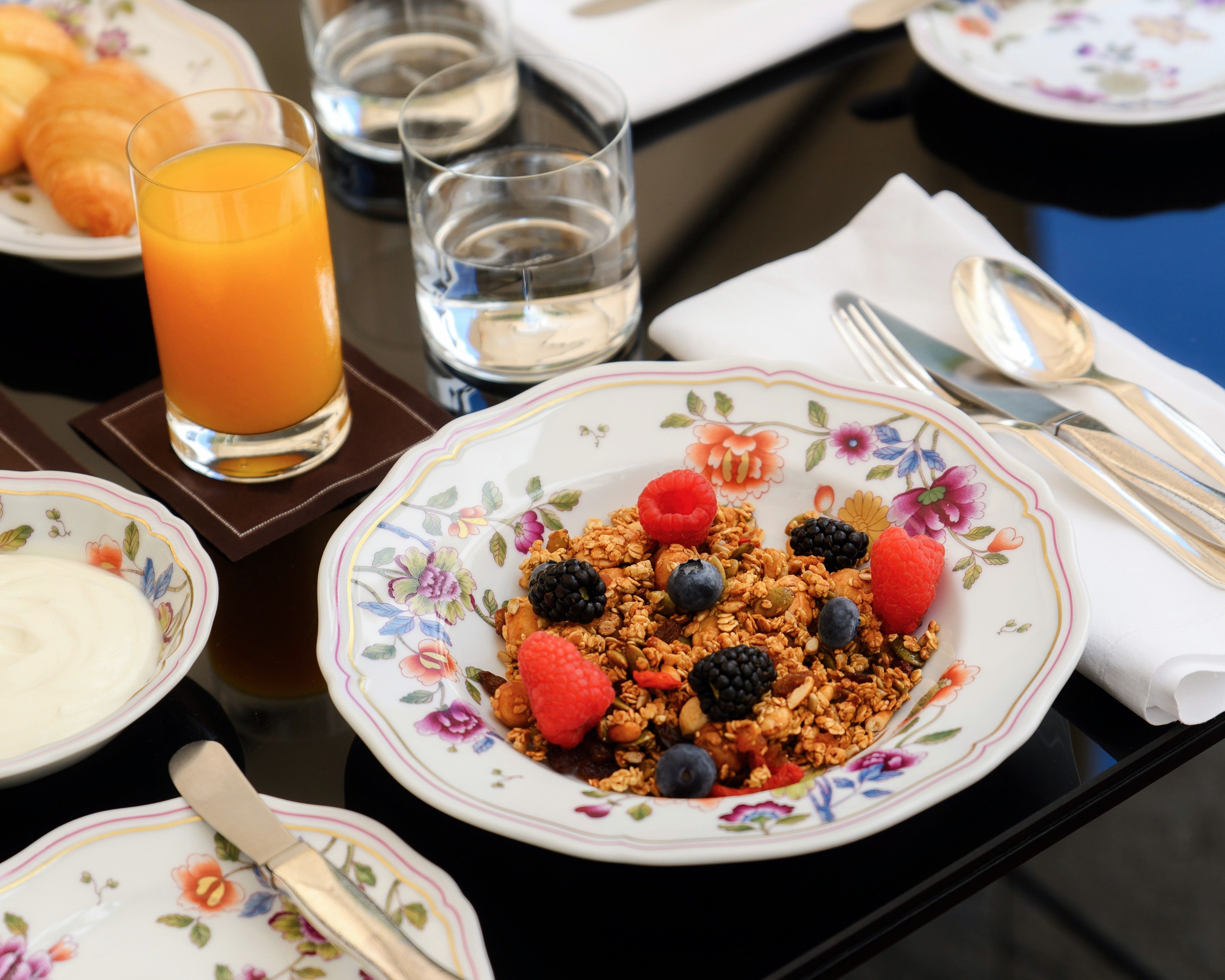 A breakfast setting with a plate of granola topped with berries, a glass of orange juice, and a bowl of yogurt.