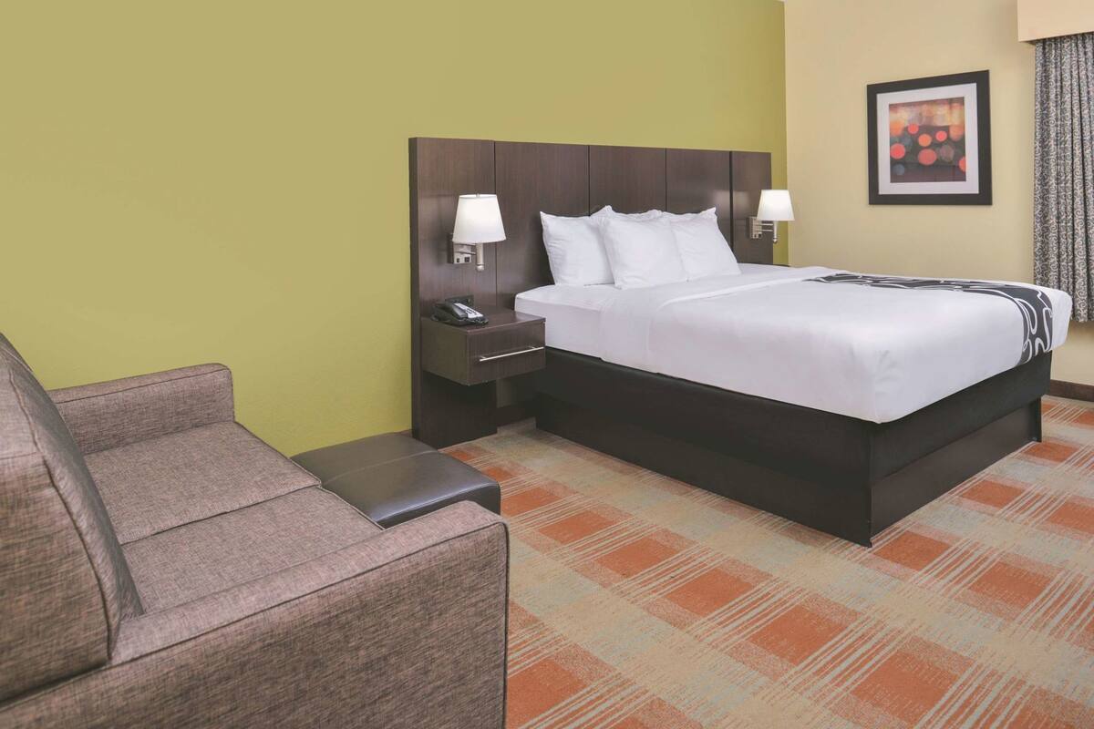 Ein Hotelzimmer mit einem Bett, einem Nachttisch, einem Sessel und einem gemusterten Teppich.